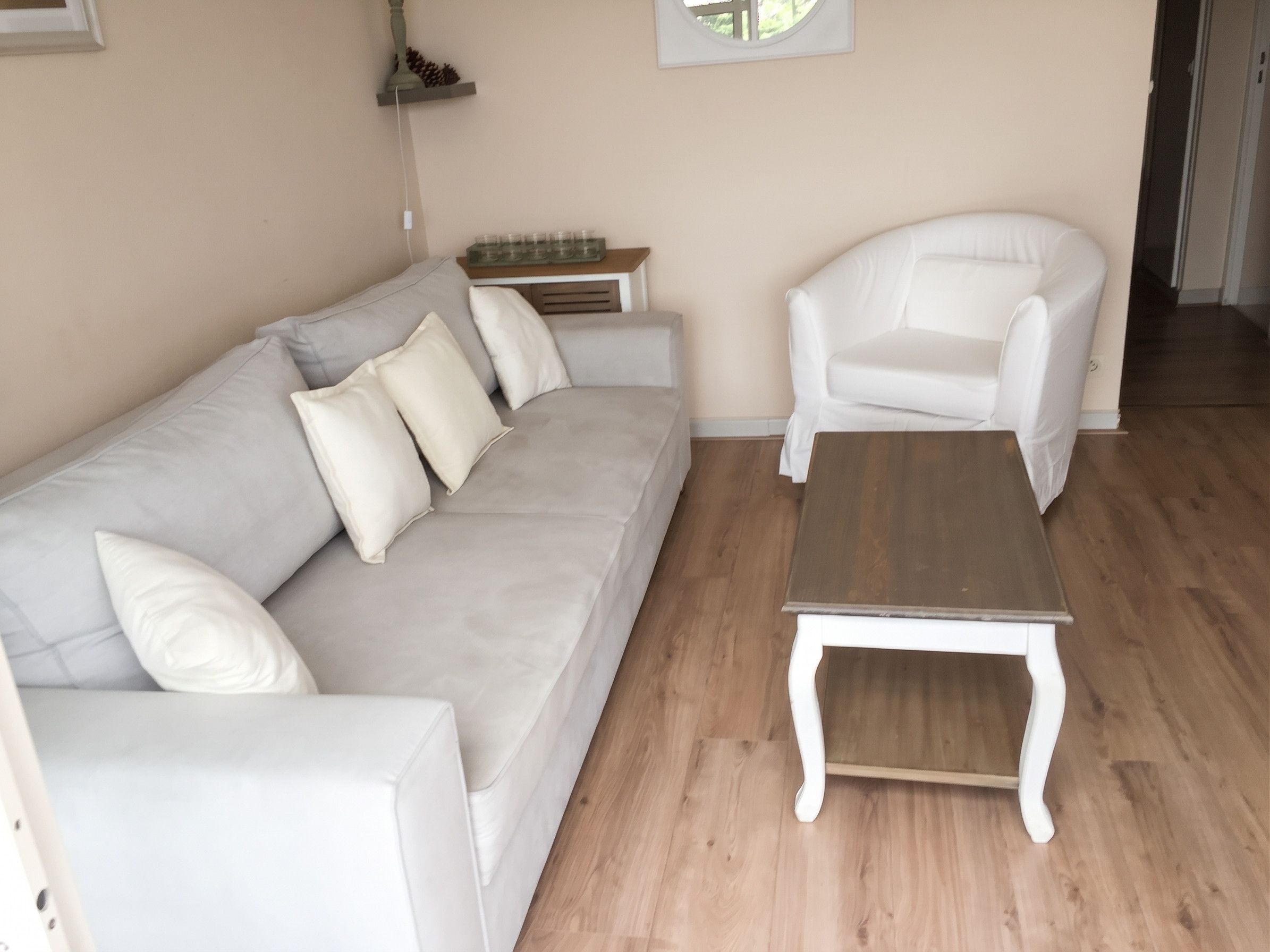 Een woonkamer met een grijze bank, witte fauteuils en een houten salontafel.
