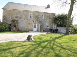 Um edifício de pedra com porta branca, uma pequena janela e um jardim com mesa e cadeiras.