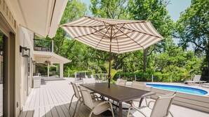 A deck with a table and chairs, a pool, and a large umbrella.