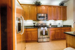 A kitchen with wooden cabinets, stainless steel appliances, and a tiled floor. - Spacious 3BR Condo near Convention & Theme Parks (Orlando)