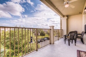 A balcony with a view of a parking lot and trees, a ceiling fan, and two chairs.