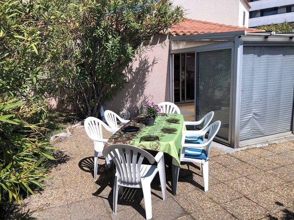 An outdoor patio with a table set for four, surrounded by white chairs.