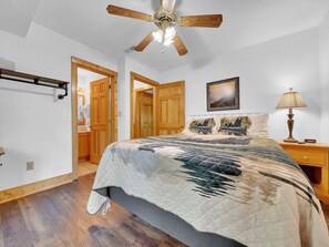 Un dormitorio con una cama grande, puertas de madera, ventilador de techo y una mesita de noche con lámpara.