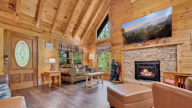 Interior acogedor de una cabaña con chimenea de piedra, paredes de madera, un ventanal grande y un espacio de estar cómodo.