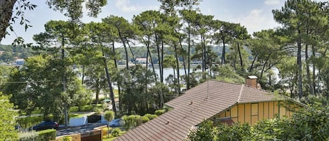 A house with a tiled roof, surrounded by trees and a body of water in the background.
