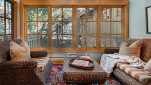 A cozy room with wicker furniture, a large window with a view of trees, and a patterned rug.