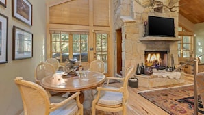 A dining area with a stone fireplace, wicker chairs, and a round table.