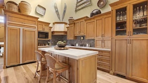 A kitchen with wooden cabinets, a central island with chairs, a microwave, and decorative items on the wall.