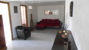 A living room with a red sofa, a black leather chair, and a wooden coffee table. There is a large mirror on the wall and a Buddha statue on the floor. - RENTAL GITE BELOW VILLA (L'escarène)