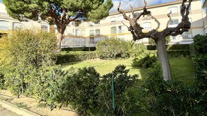 A courtyard with a large tree, a sculptural tree, and a building with balconies in the background. - Cozy Studio Near Beach, Shops, Private Garage, Pet-Friendly, Sleeps 4 (Argelès-sur-Mer)