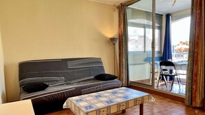 A room with a sofa, a small table, and a view through a glass door to an outdoor area with chairs. - Cozy Studio Near Beach, Shops, Private Garage, Pet-Friendly, Sleeps 4 (Argelès-sur-Mer)