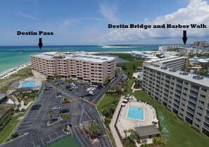 An aerial view of a hotel complex with a pool, parking lot, and a view of the ocean.