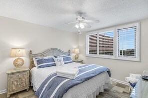 A bedroom with a bed, nightstands, a ceiling fan, and a window with blinds.