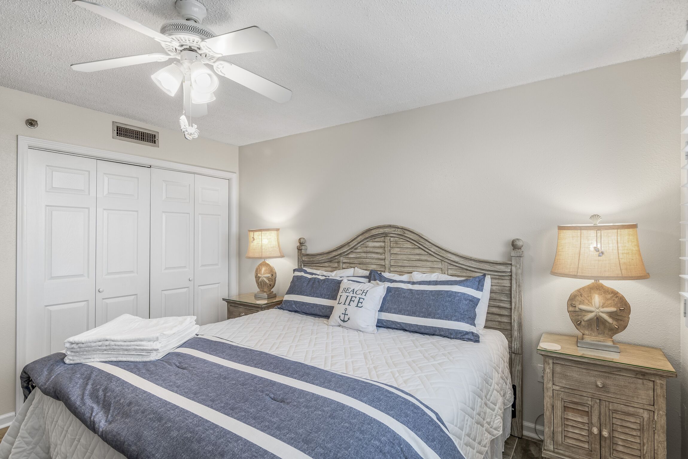 A bedroom with a bed, two bedside tables, a ceiling fan, and a door.