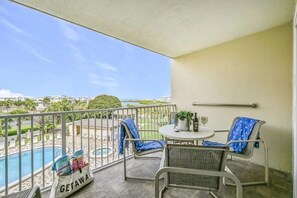 A balcony with a pool view, wicker chairs, a small table with a plant and wine glasses, and a 'GETAWAY' bag.