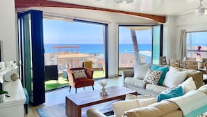 A spacious living room with a large sliding glass door leading to a balcony with a view of the ocean. There is a white sofa, a wooden coffee table, and a brown armchair. - Beach View Pet Friendly Home with a Spa Pe-1722 (Oceanside)