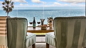 A view from a balcony overlooking the sea, featuring two upholstered chairs, a bottle of wine, glasses, and a small table with a decorative item. - Beach View Pet Friendly Home with a Spa Pe-1722 (Oceanside)