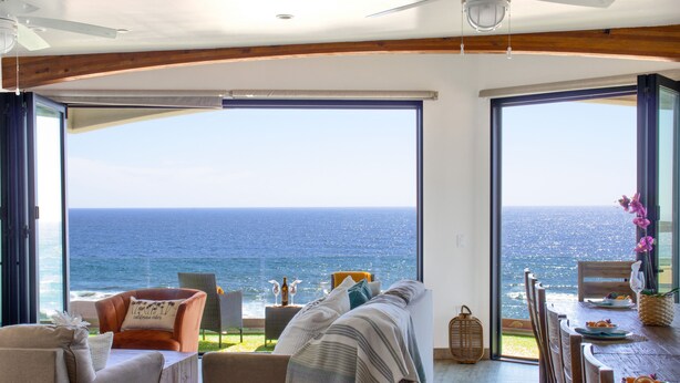 A room with a large sliding glass door leading to a balcony with a view of the ocean. Inside, there is a sofa, a dining table with chairs, and a small side table with decorative items. - Beach View Pet Friendly Home with a Spa Pe-1722 (Oceanside)