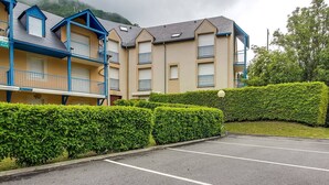 A multi-story hotel with balconies, a parking lot, and a well-maintained hedge. - Calm T3 for 6, terrace, garden, near amenities (Esquièze-Sère)