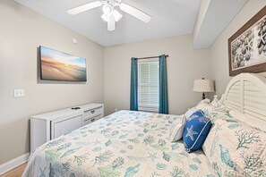 A bedroom with a bed, a ceiling fan, a window with curtains, a wall-mounted picture, and a bedside table with a lamp. - Breath-taking panoramic ocean & beach views (Destin)