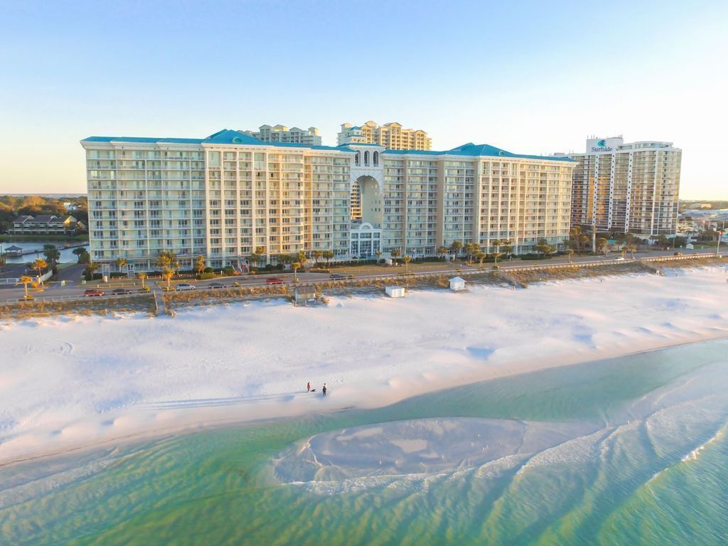 Een groot hotel met meerdere verdiepingen, een centrale binnenplaats en een strandgedeelte met helder water.
