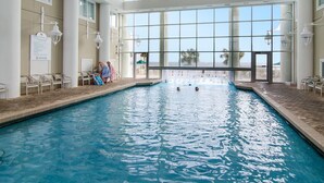 Une piscine intérieure avec des parois en verre transparent, un sol carrelé et un panneau indiquant qu’il est interdit de plonger.