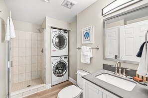 A compact bathroom with a shower, a washing machine, a toilet, and a sink. - Breath-taking panoramic ocean & beach views (Destin)
