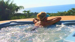 Eine Person entspannt in einer Hot-Tub mit Blick auf das Meer und üppige tropische Vegetation.
