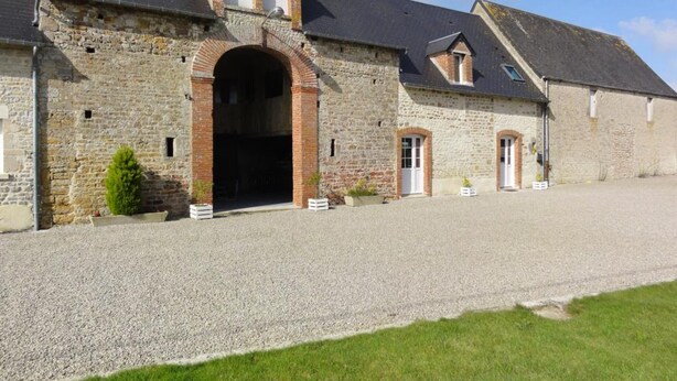 Un bâtiment en pierre doté d’une grande entrée en arc de cercle, d’une allée gravillonnée et d’une pelouse devant.