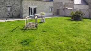 Un bâtiment en pierre avec un toit en pente, une terrasse en bois et une cour gazonnée.