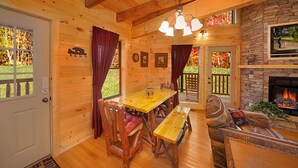 Interior de una cabaña de madera con una mesa de comedor, bancos y una chimenea.