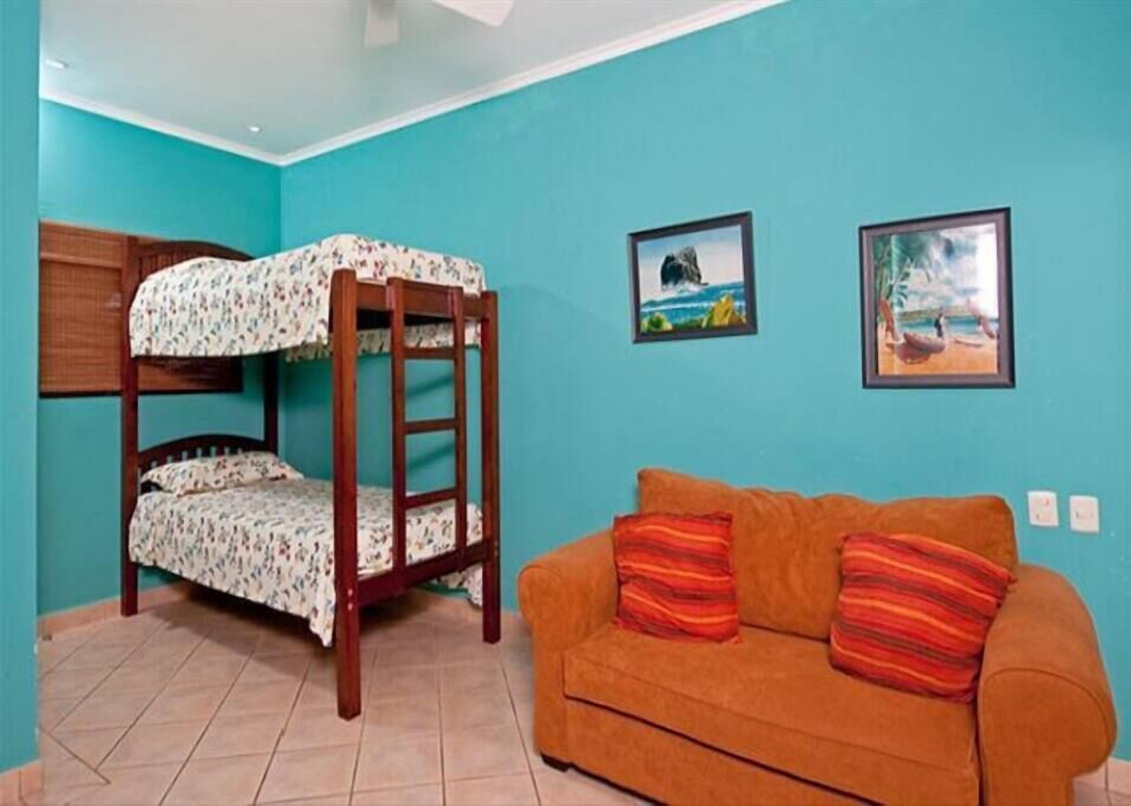Una habitación con literas y un sofá naranja con cojines a rayas.