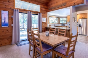 A wooden cabin interior with a dining area, kitchen, and large windows.