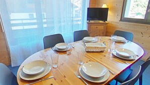 Een eetruimte met een ronde houten tafel, gedekt voor zes personen, omringd door stoelen.