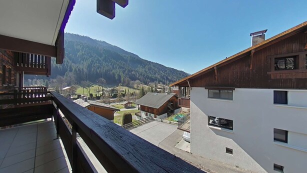 Een balkon met uitzicht op een bergachtig landschap, houten gebouwen en een heldere lucht.