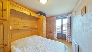 Een kamer met houten lambrisering, een bed met wit beddengoed, een plafondlamp, een raam met gordijnen en een radiator.