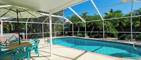 A covered swimming pool with a patio area, including chairs and a table.