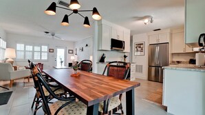 A modern kitchen with white cabinets, a stainless steel refrigerator, and a dining area with a wooden table and wicker chairs. - 217 84th - Anna Maria Island- Private home 3 Bedroom/ 2 Bath with private pool , maximum occupancy of 6 people. (Holmes Beach)