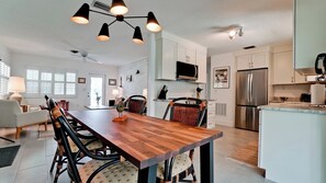 A modern kitchen with white cabinets, a stainless steel refrigerator, and a dining area with a wooden table and wicker chairs.