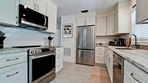 A modern kitchen with white cabinets, stainless steel appliances, and a tiled backsplash. - 217 84th - Anna Maria Island- Private home 3 Bedroom/ 2 Bath with private pool , maximum occupancy of 6 people. (Holmes Beach)