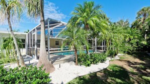A modern house with a glass conservatory, a swimming pool, and lush tropical landscaping. - 217 84th - Anna Maria Island- Private home 3 Bedroom/ 2 Bath with private pool , maximum occupancy of 6 people. (Holmes Beach)