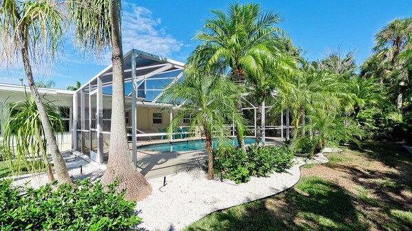 A modern house with a glass conservatory, a swimming pool, and lush tropical landscaping.