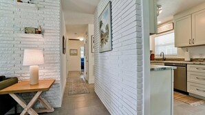 A modern kitchen with white brick walls, a dining area with a table and chairs, and a hallway leading to another room. - 217 84th - Anna Maria Island- Private home 3 Bedroom/ 2 Bath with private pool , maximum occupancy of 6 people. (Holmes Beach)