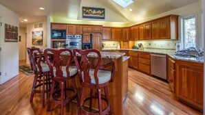 A kitchen with wooden cabinets, a central island with bar stools, a skylight, and a view of the outdoors. - CYPR10 - Huge Home, 2 Suites, Dog Friendly, Hot Tub (Sunriver)