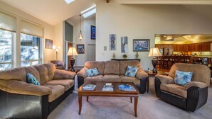 A spacious living room with a large sectional sofa, a coffee table, and a dining area with wooden cabinets and a chandelier. - CYPR10 - Huge Home, 2 Suites, Dog Friendly, Hot Tub (Sunriver)