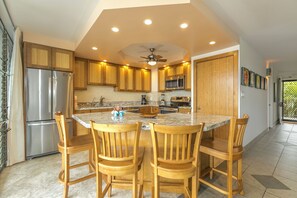Una cocina moderna con armarios de madera, un refrigerador de acero inoxidable, un microondas y una isla central con sillas.