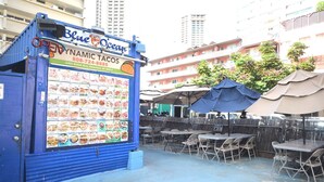 Un espace de restauration en plein air avec des tables et des chaises, un panneau affichant le menu, et des parasols.