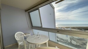 A balcony with a table and chairs, overlooking a beach and a road.