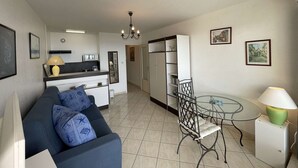 A modern apartment with a kitchenette, a dining area with a glass table, a sofa with patterned cushions, and a chandelier.