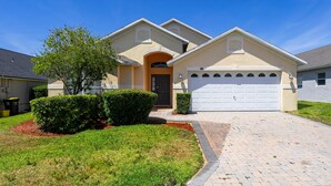Una casa a due piani con facciata beige, una porta d'ingresso scura e un portone del garage bianco.
